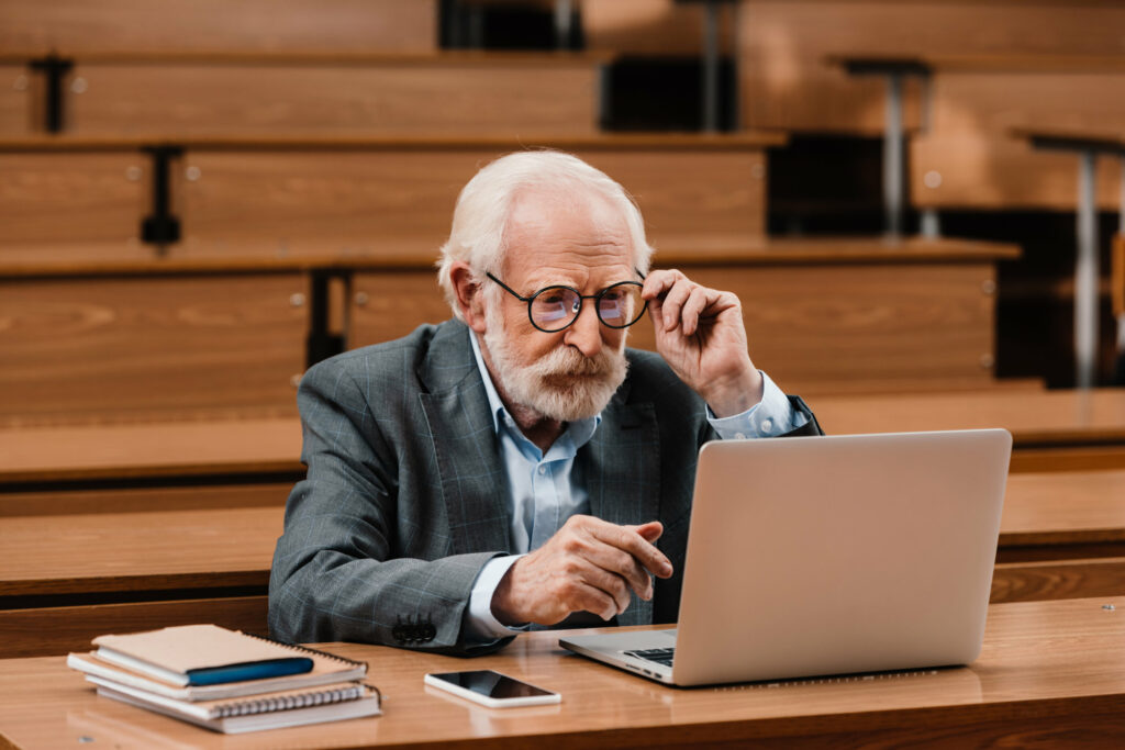 grey hair older looking professor looking at laptop